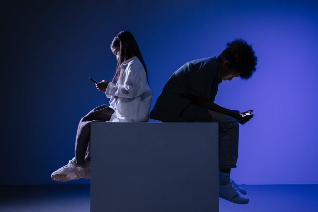 Silhouettes of kids using smartphones on a block, set against blue studio lighting.